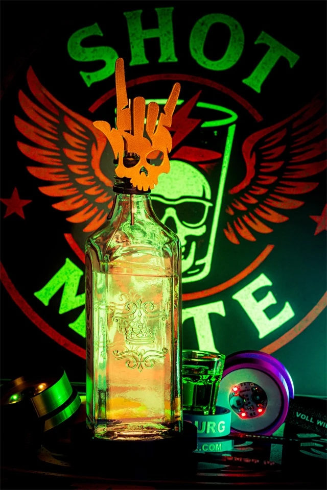 Flasche mit Totenkopf-Rockeraufsatz vor SHOT MATE Logo, daneben leuchtender LED-Spinner und Shotglas.